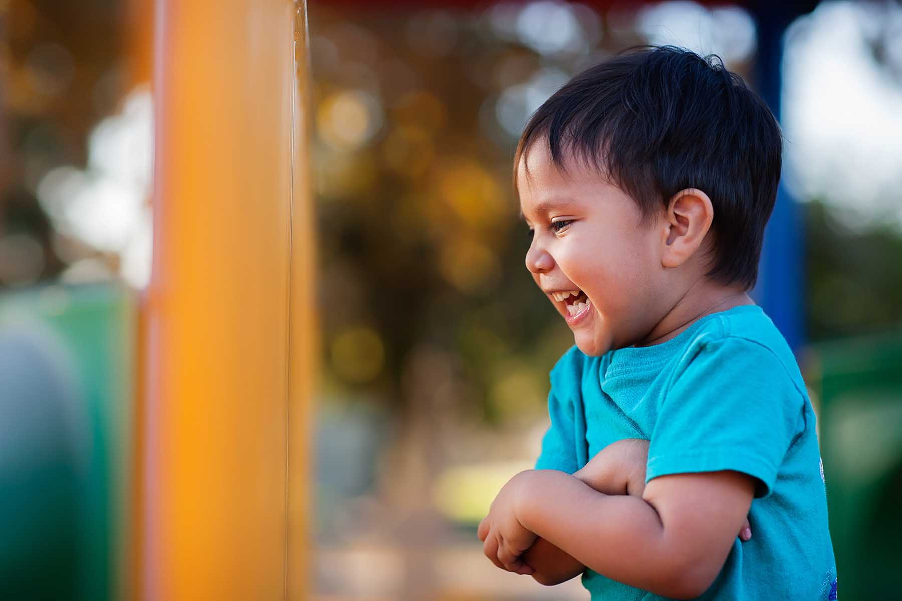 Young boy laughing out loud and holding his arms together while playing in a jungle gym.