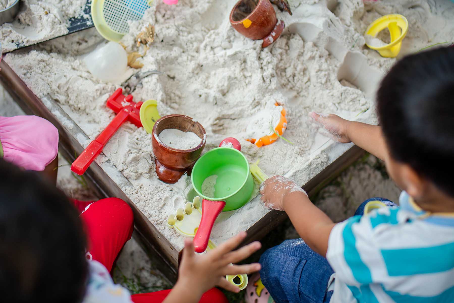 Children playing in a sandbox with a variety of tools