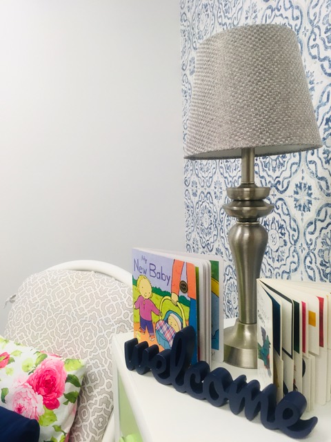 A bedside table with a silver lamp with two baby books on it