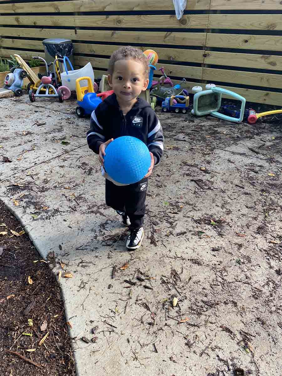 A young boy in a black jacket and a blue ball at Community School for People Under Six in Carrboro, NC