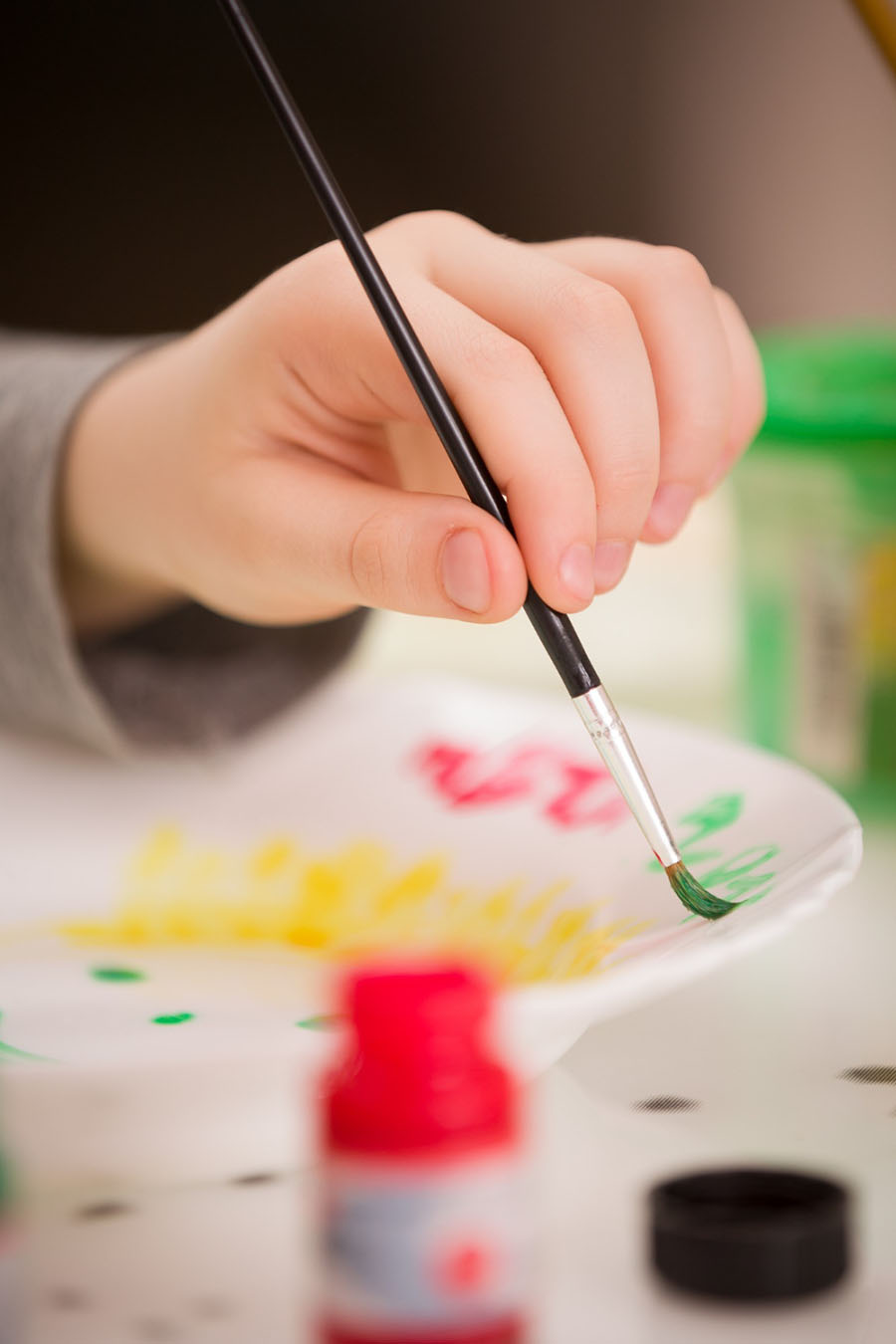 Small child sitting at a table painting a plate