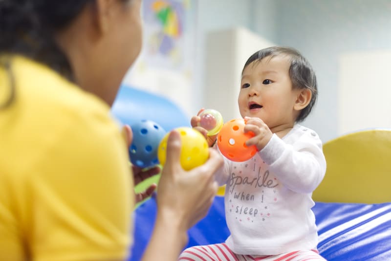 A baby plays a game with balls with an older person in a yellow shirt